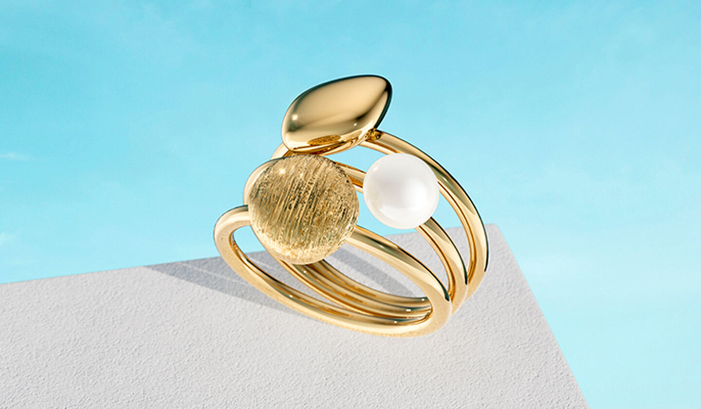 Birks Pebble gold and pearl ring on a blue background.